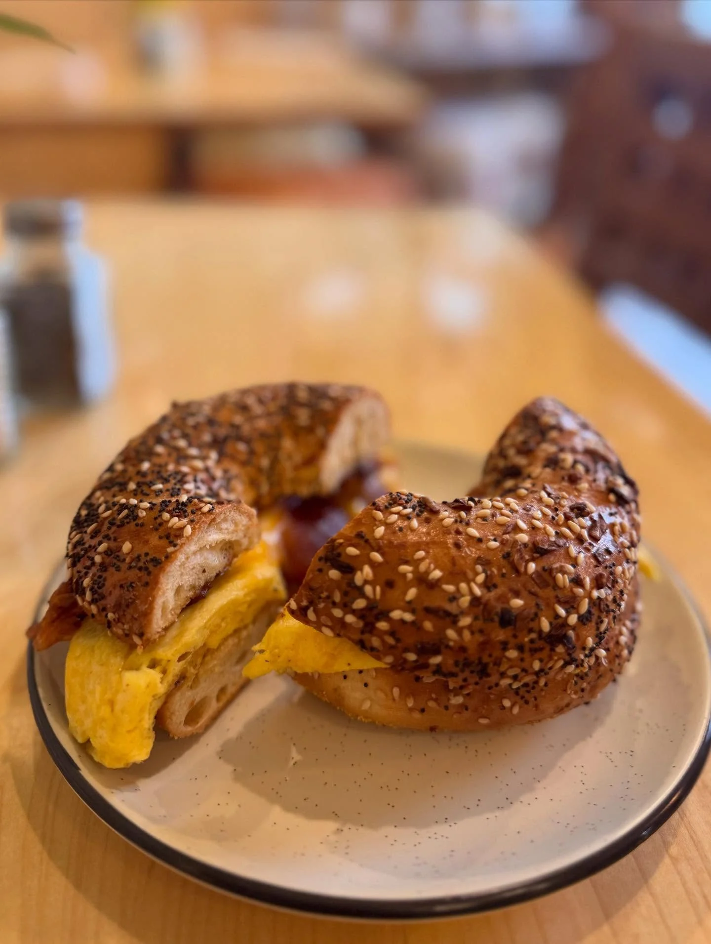 Everything bagel breakfast sandwich filled with egg and bacon, cut in half on a plate