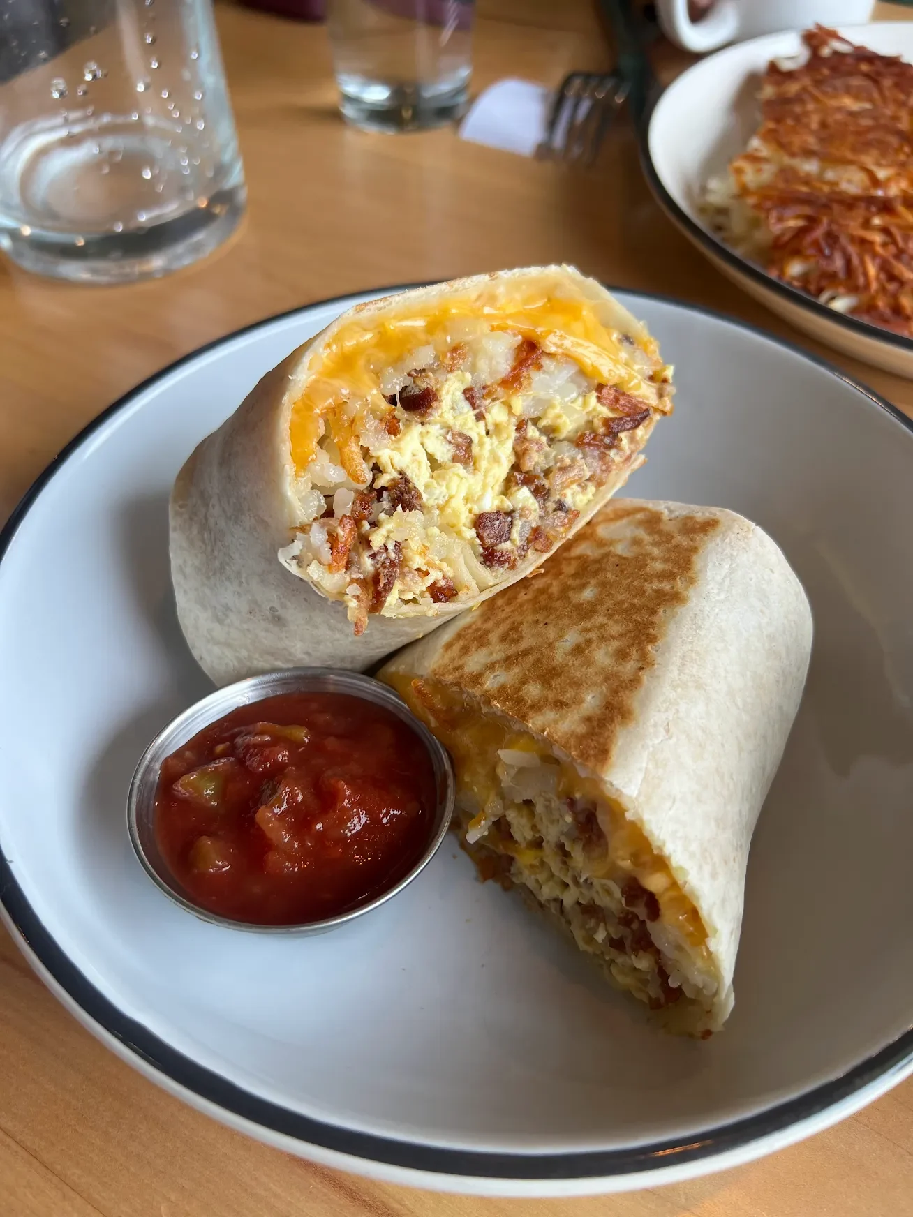 Breakfast burrito with scrambled eggs, sausage, and cheese served with salsa and sour cream on a white plate