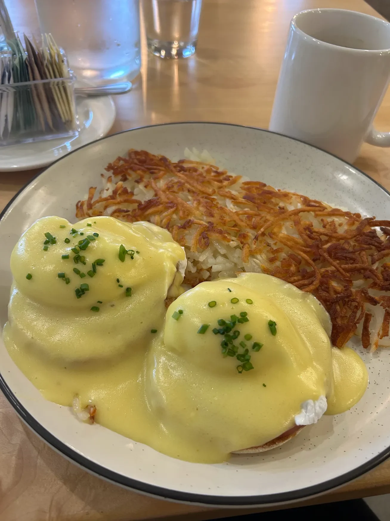 Eggs Benedict with hollandaise sauce served with crispy hash browns on a plate
