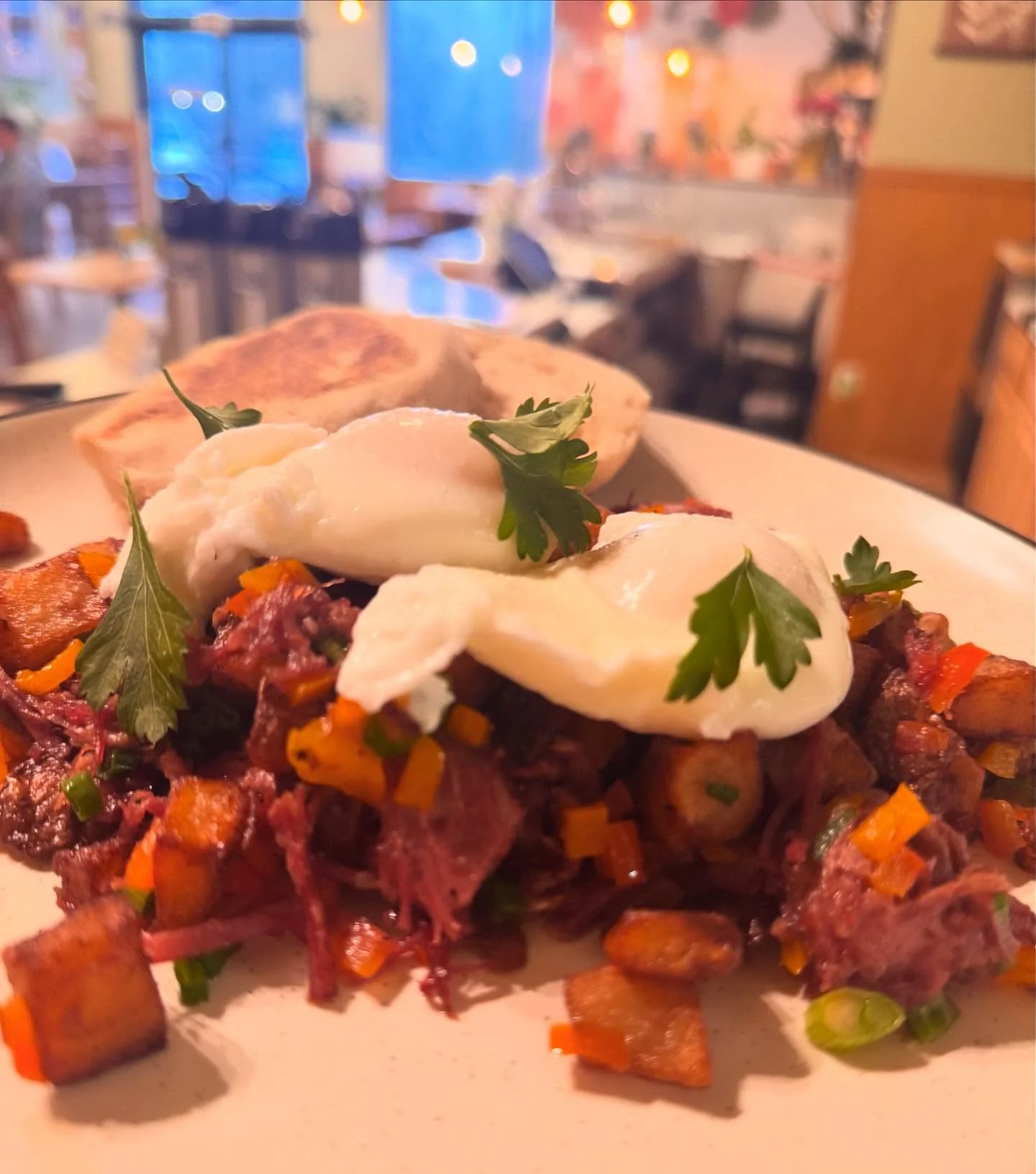 Corned beef hash topped with poached eggs, diced vegetables, and toasted English muffin