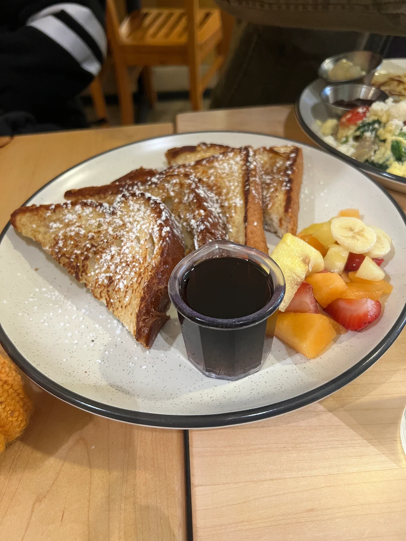Powdered sugar French toast with fresh strawberries, banana slices, and syrup, served with a glass of orange juice