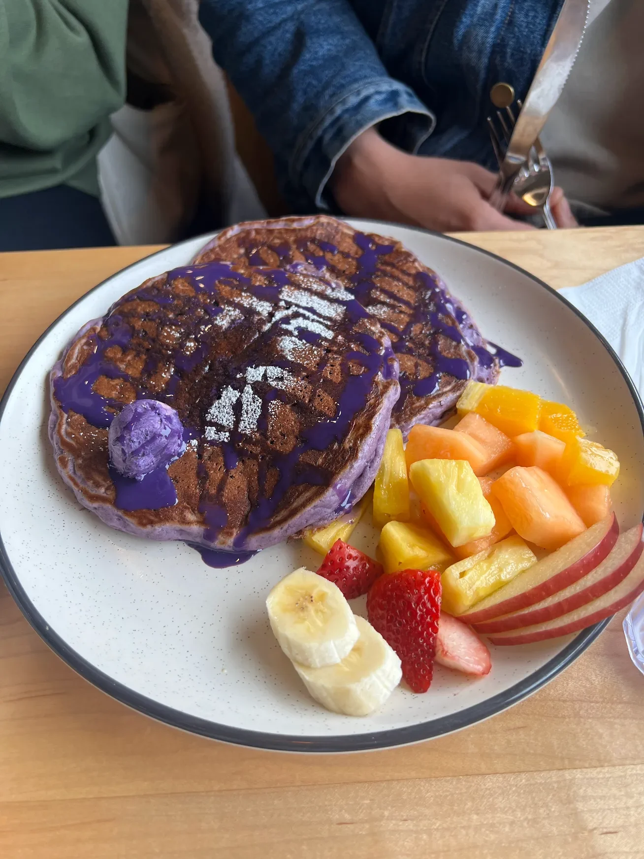 Ube pancakes topped with purple sauce served with fresh fruit on a plate